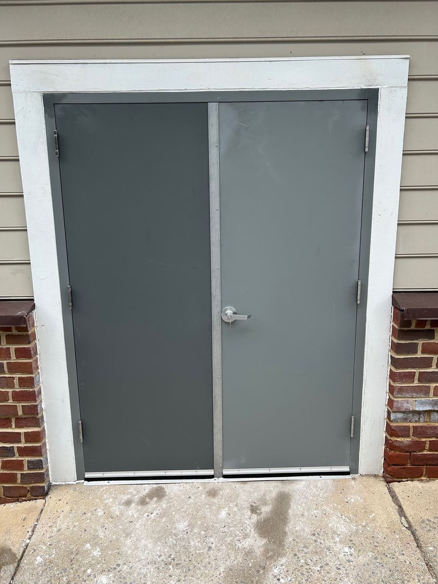 The replacement commercial hollow metal door and frame installed in the same opening, unpainted grey primer finish with new push hardware.