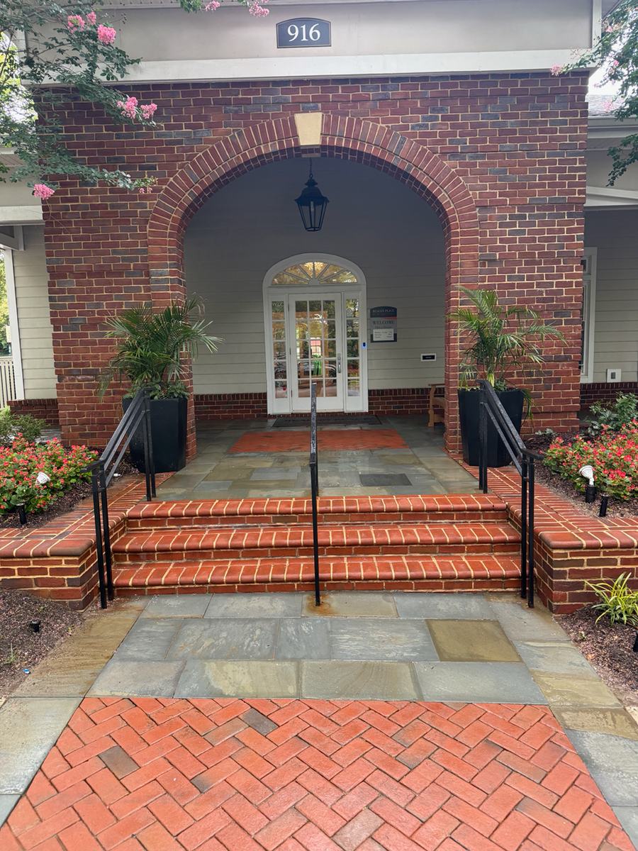 The completed leasing office entrance: a brick arch over a glass door, with cleaned flagstone landing, red brick paving and planted urns on either side.