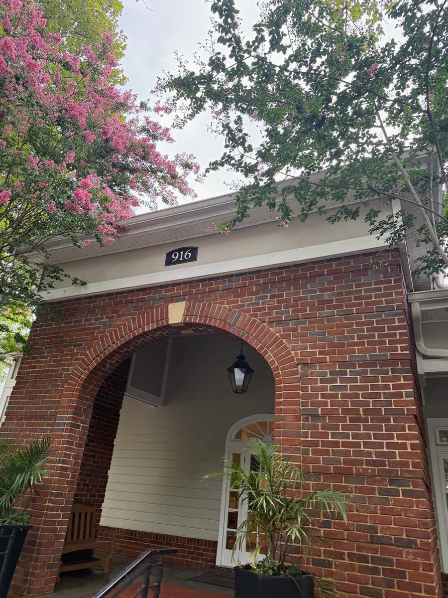 The restored brick facade and entrance arch of the leasing office, with a crape myrtle in bloom in front of the cleaned brickwork and soffit.