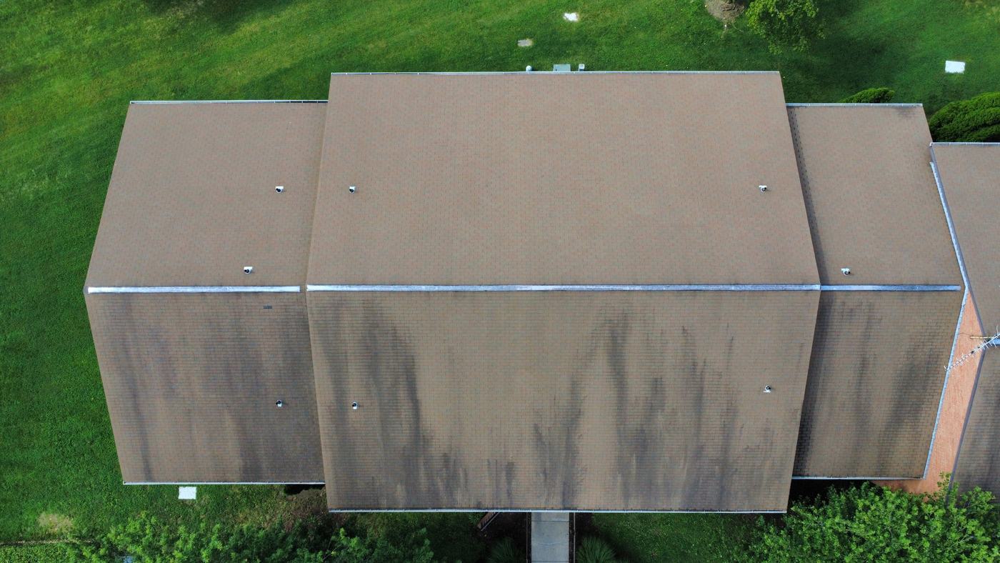 Close overhead view of a shingle roof showing pronounced dark streaking and color fading consistent with granule loss across the whole field.